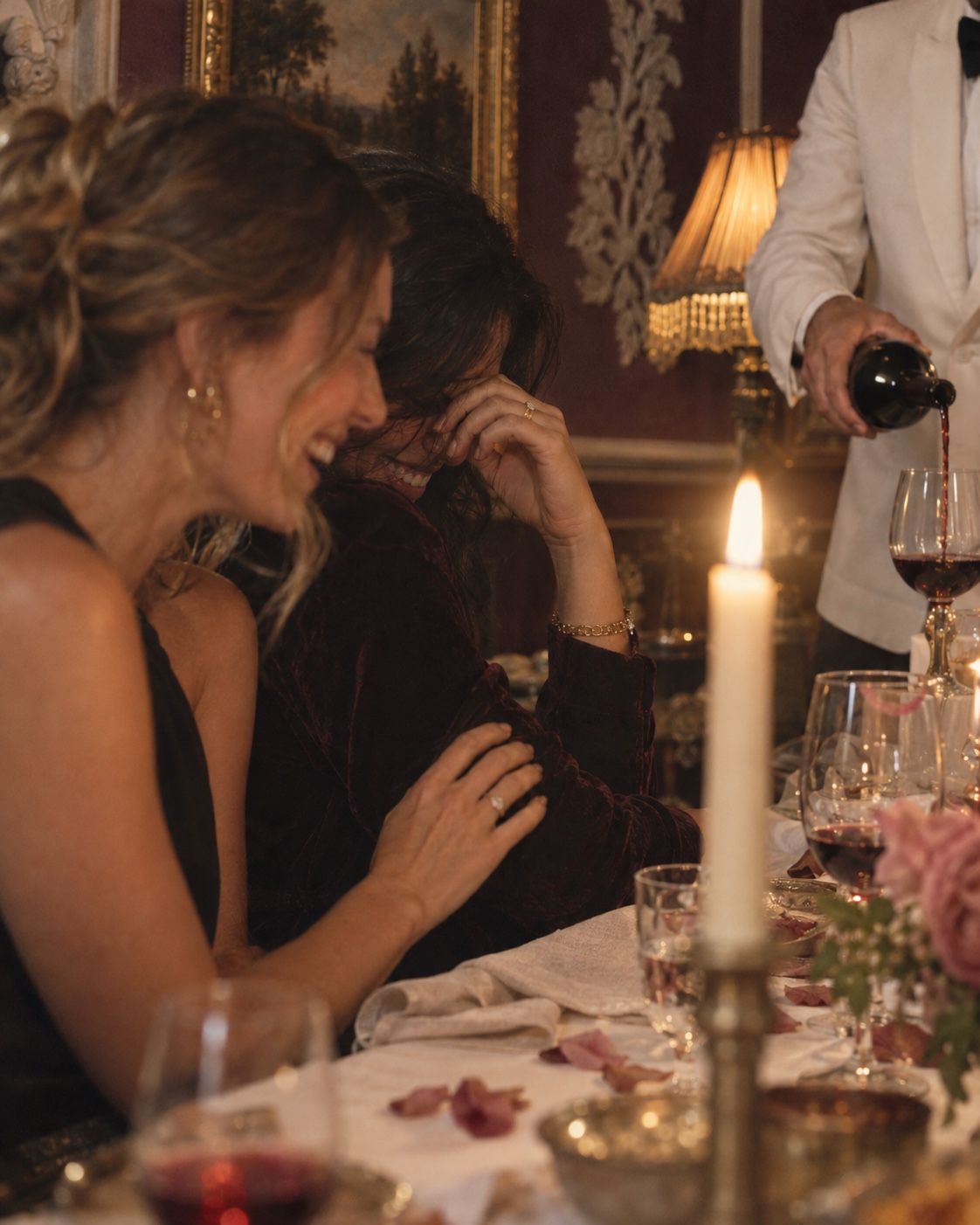 Guests laughing at the table as a waiter pours red wine